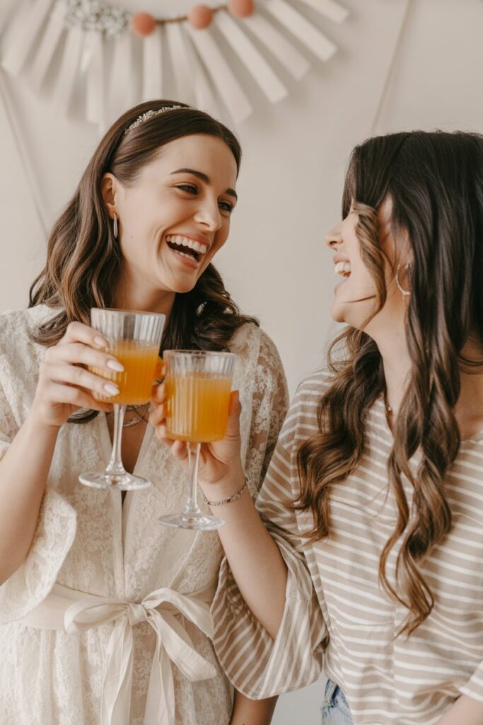 A joyous bride-to-be laughing and raising a glass, celebrating her engagement in a beautiful outfit.15 Stylish Engagement Outfit Ideas For Every Bride-To-Be